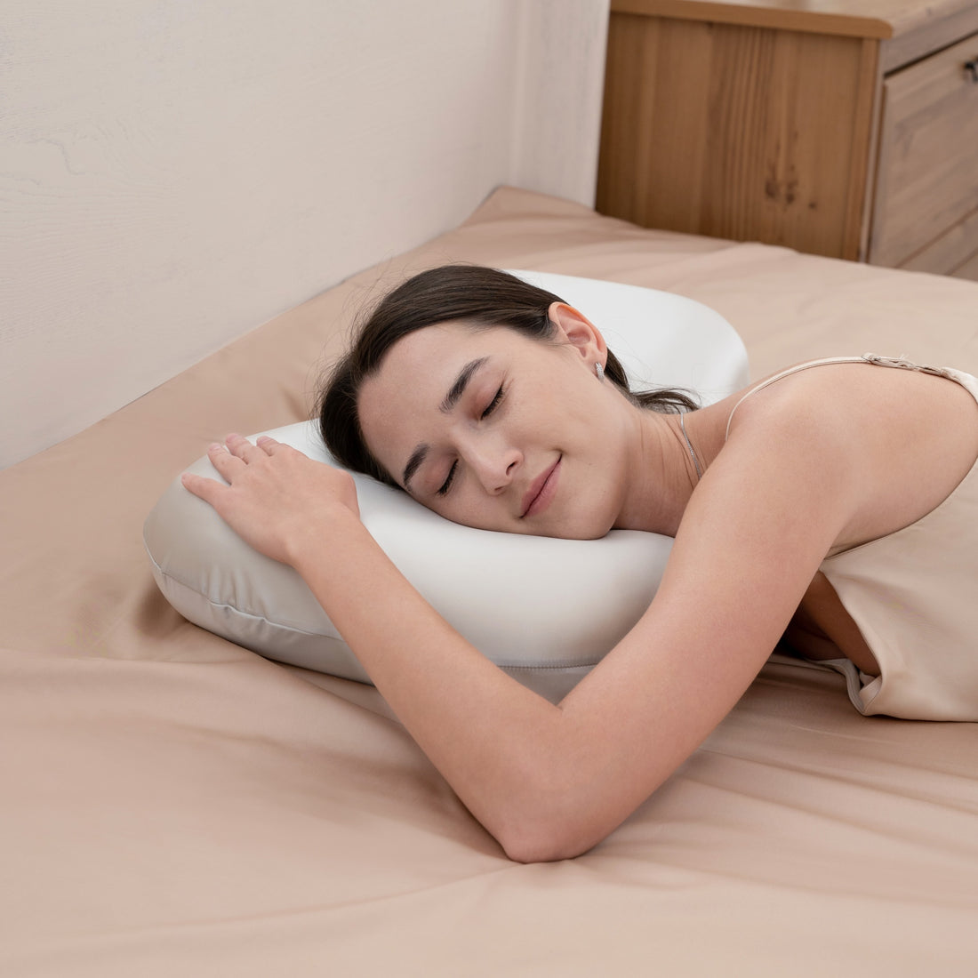 White ergonomic pillow on a bed with a wooden dresser in the background