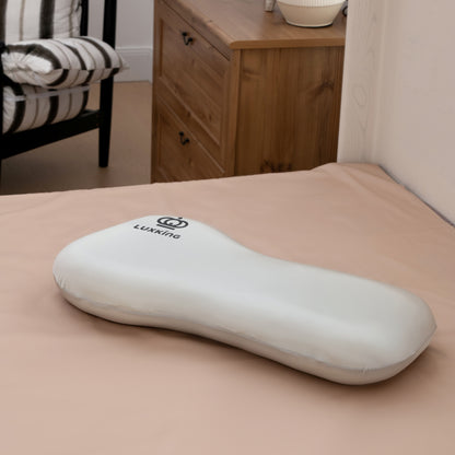 White ergonomic pillow on a bed with a wooden dresser in the background