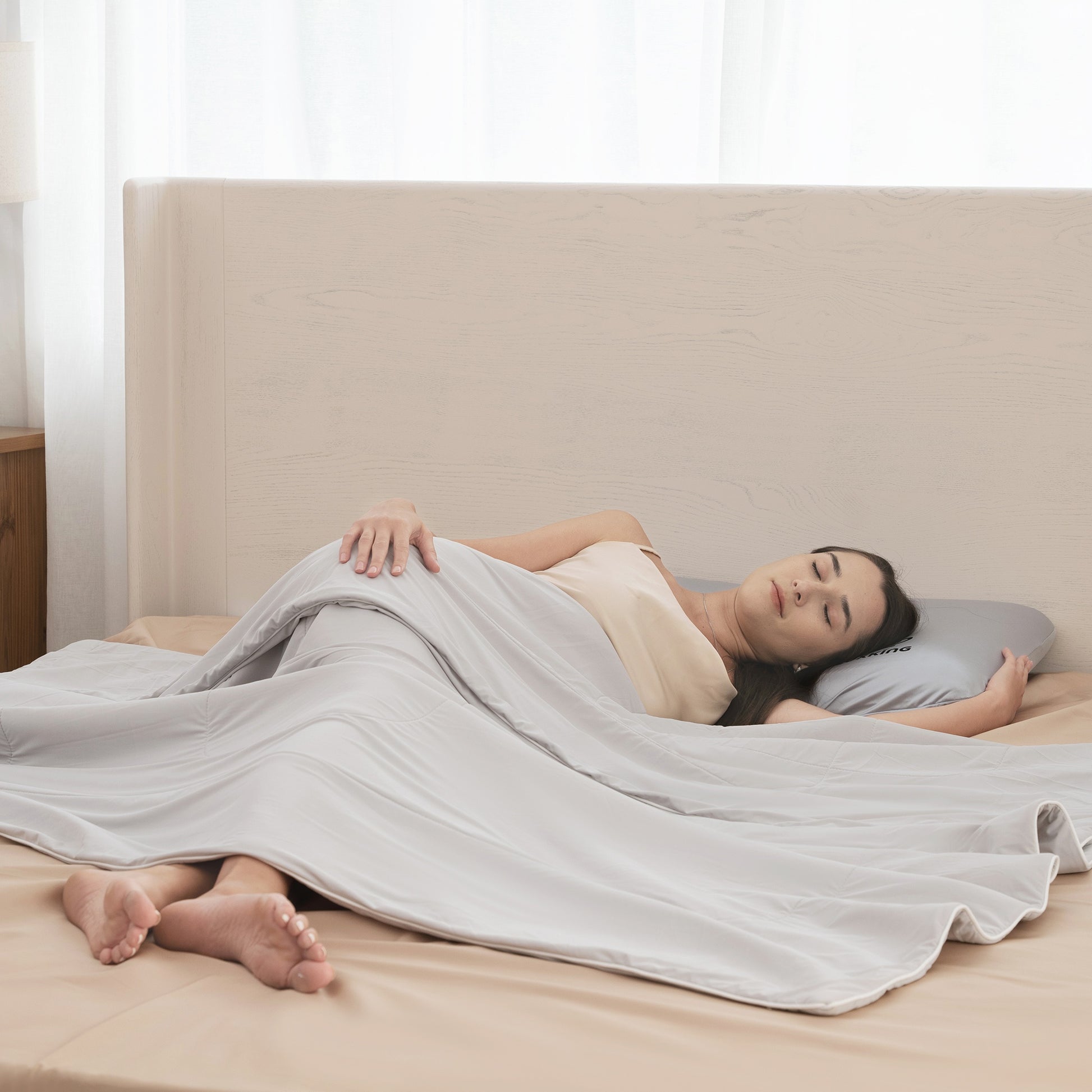 Woman lying on a bed under a white blanket in a bright bedroom.