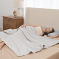 Woman lying in bed under a gray blanket in a bedroom setting.