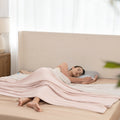 Woman lying in bed with a pink blanket and using a smartphone.