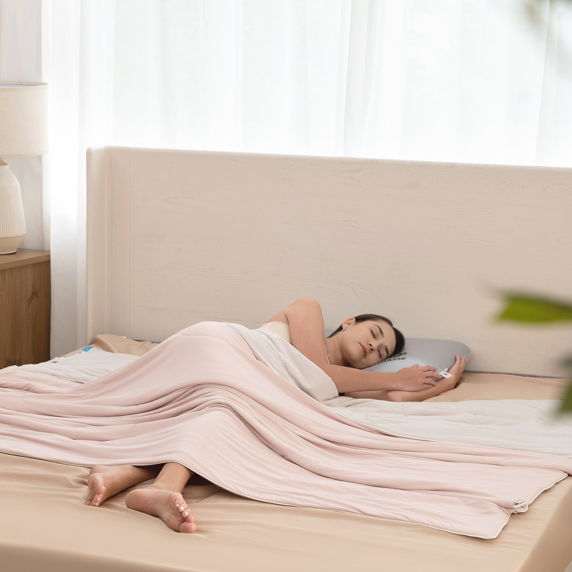 Woman lying in bed with a pink blanket and using a smartphone.