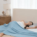 Woman lying in bed under a blue blanket in a bedroom setting.