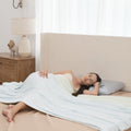 Woman lying on a bed with a white blanket and pillow, in a bedroom setting.
