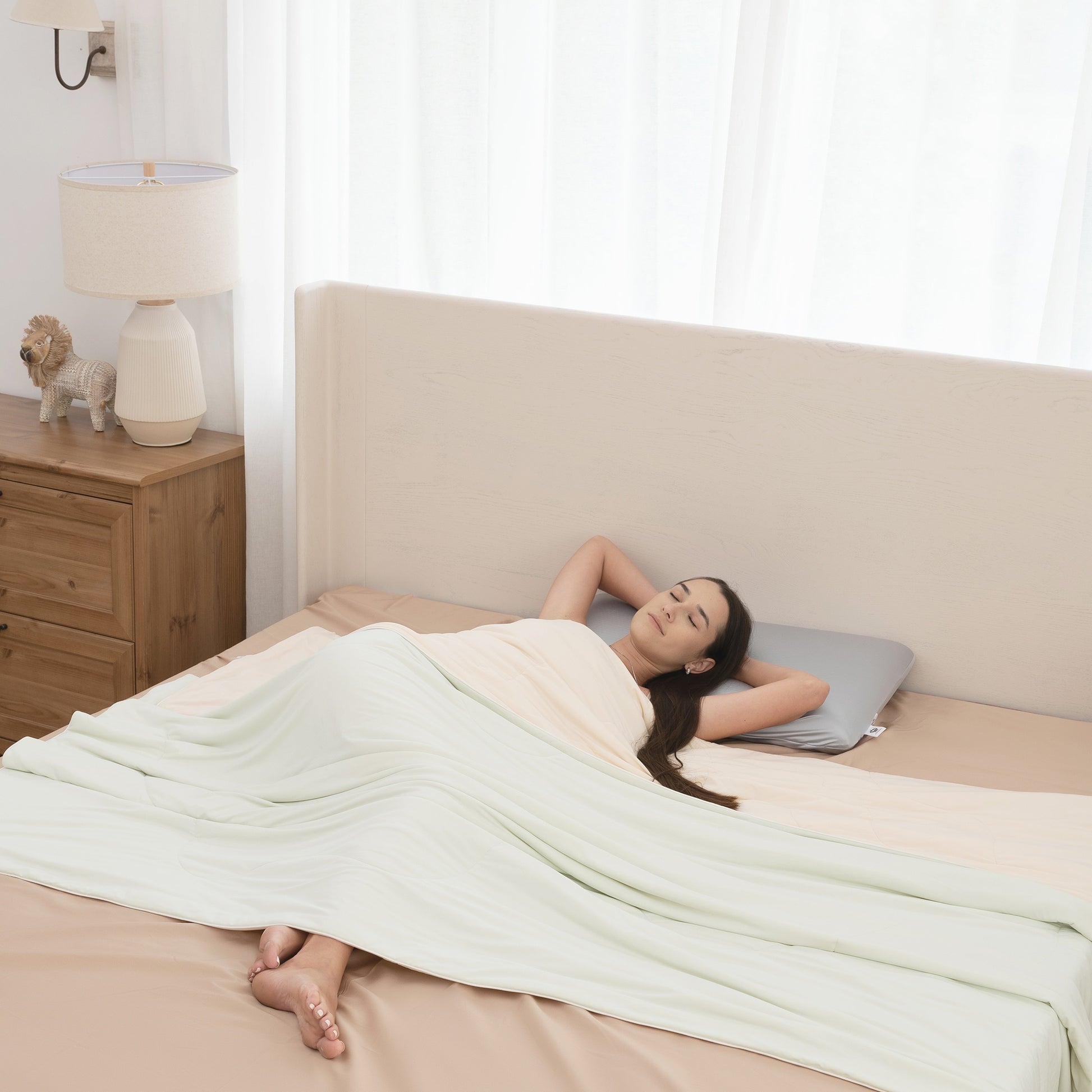 Woman lying on a bed with a white blanket in a bright bedroom.
