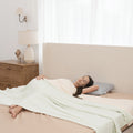 Woman lying on a bed with a white blanket and pillow, in a bedroom setting.