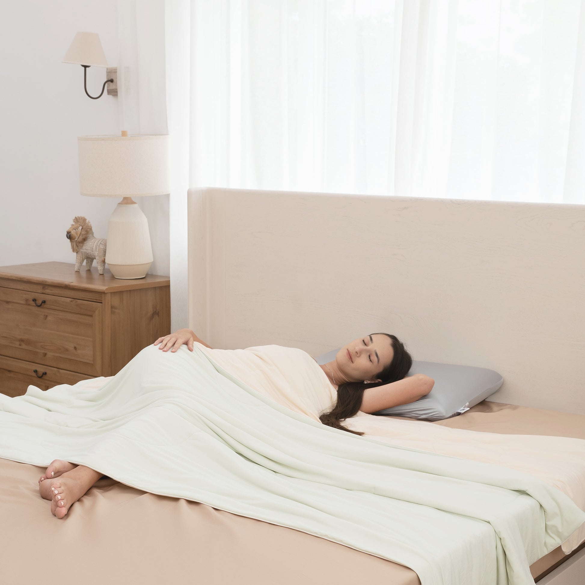 Woman lying on a bed with a white blanket and pillow, in a bedroom setting.
