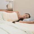 Woman sleeping peacefully under a light green comforter in a softly lit bedroom.